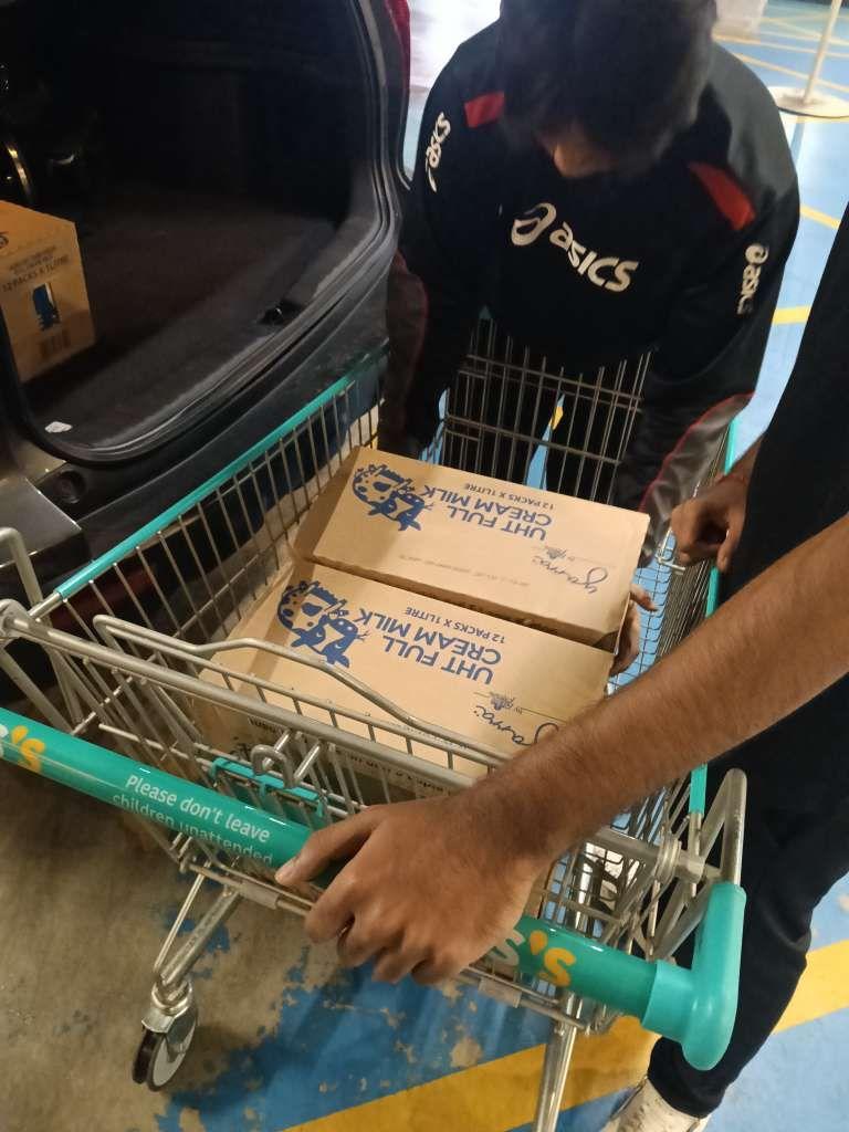 UHT full cream milk boxes being moved from a shopping trolley into a car boot.