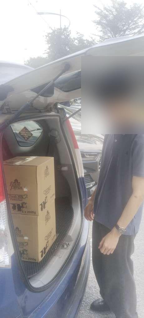 Farm Fresh milk cartons being loaded into a car boot after delivery, in a car park.